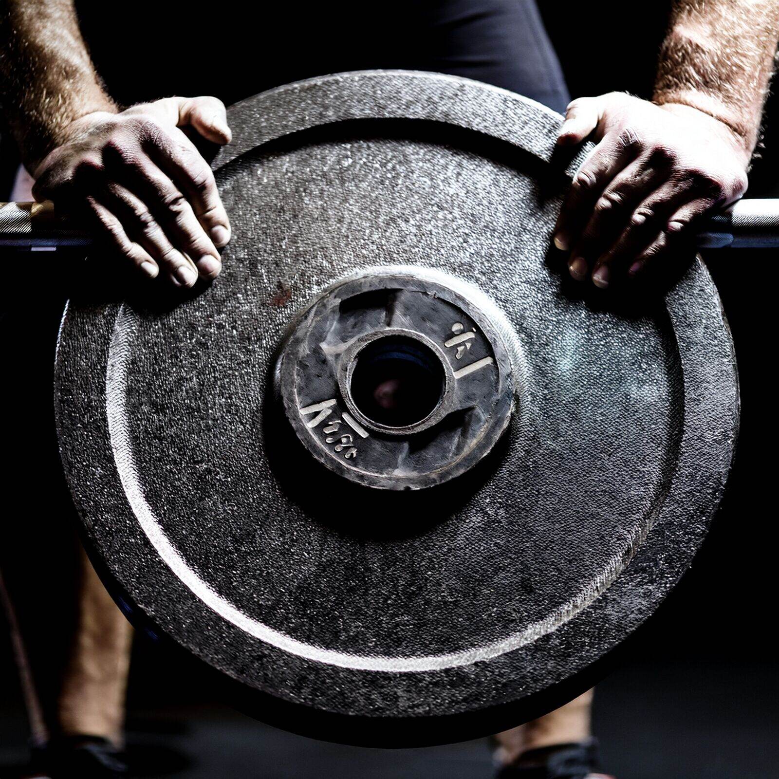Hands on a loaded barbell, the centre bore of the weight plate visible